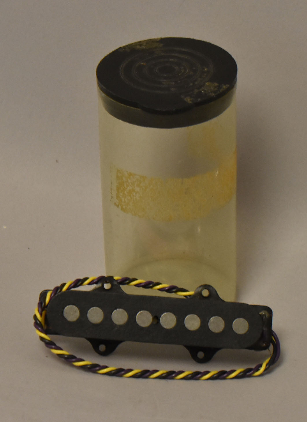 A black 8-pole bass pickup with yellow and purple braided wire, shown with a clear plastic tube and black cap behind it.