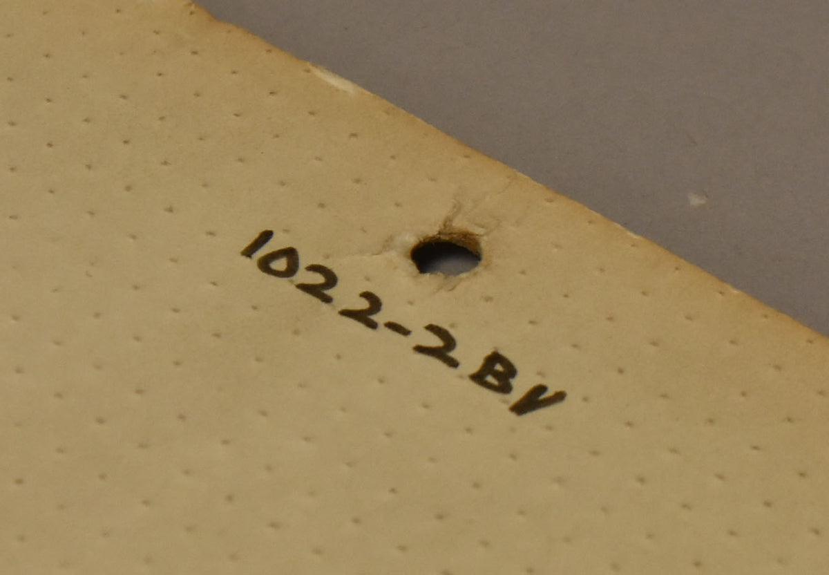 Close-up of the back of the black pickguard, showing a cream-colored textured surface with a small hole and handwritten numbers.