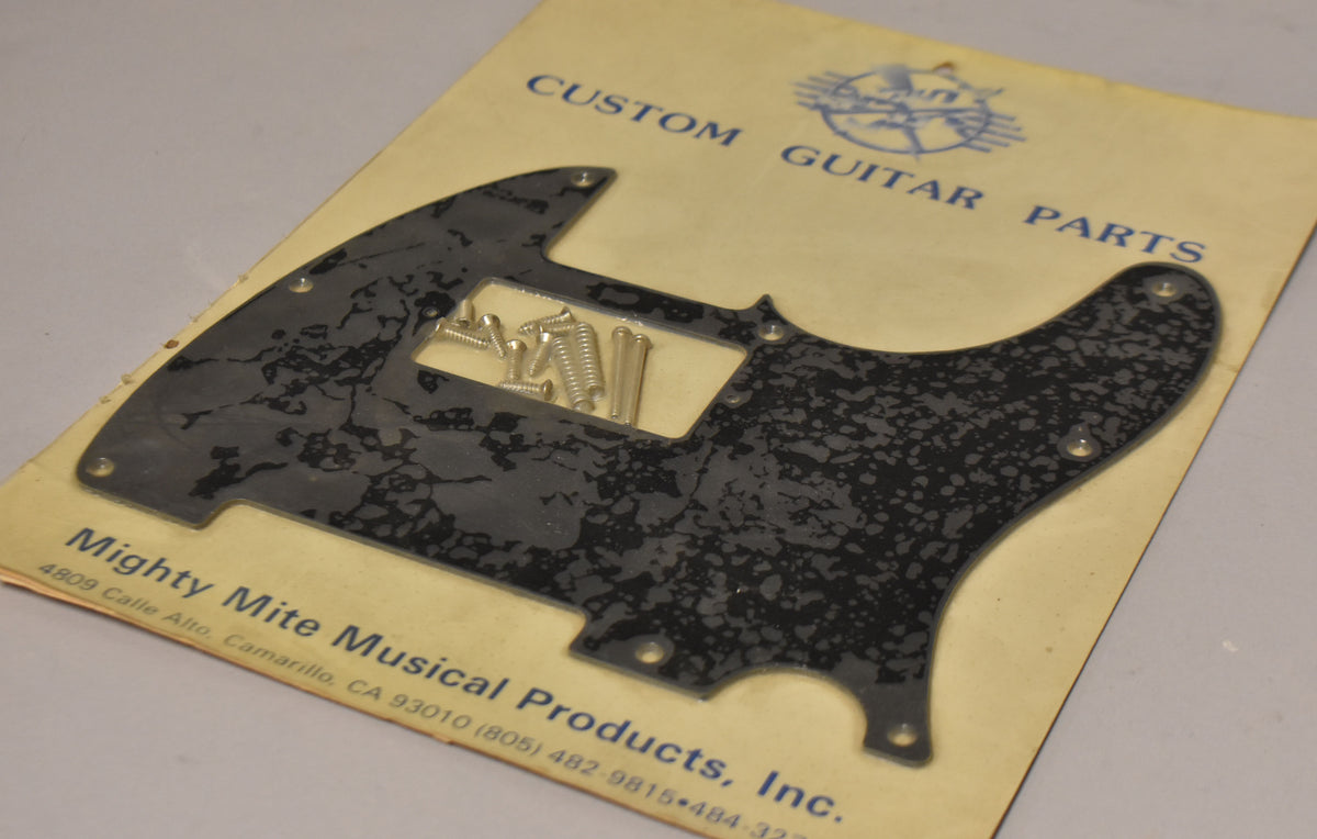 A black mottled pickguard with a humbucker cutout, still sealed in its original packaging with mounting screws.