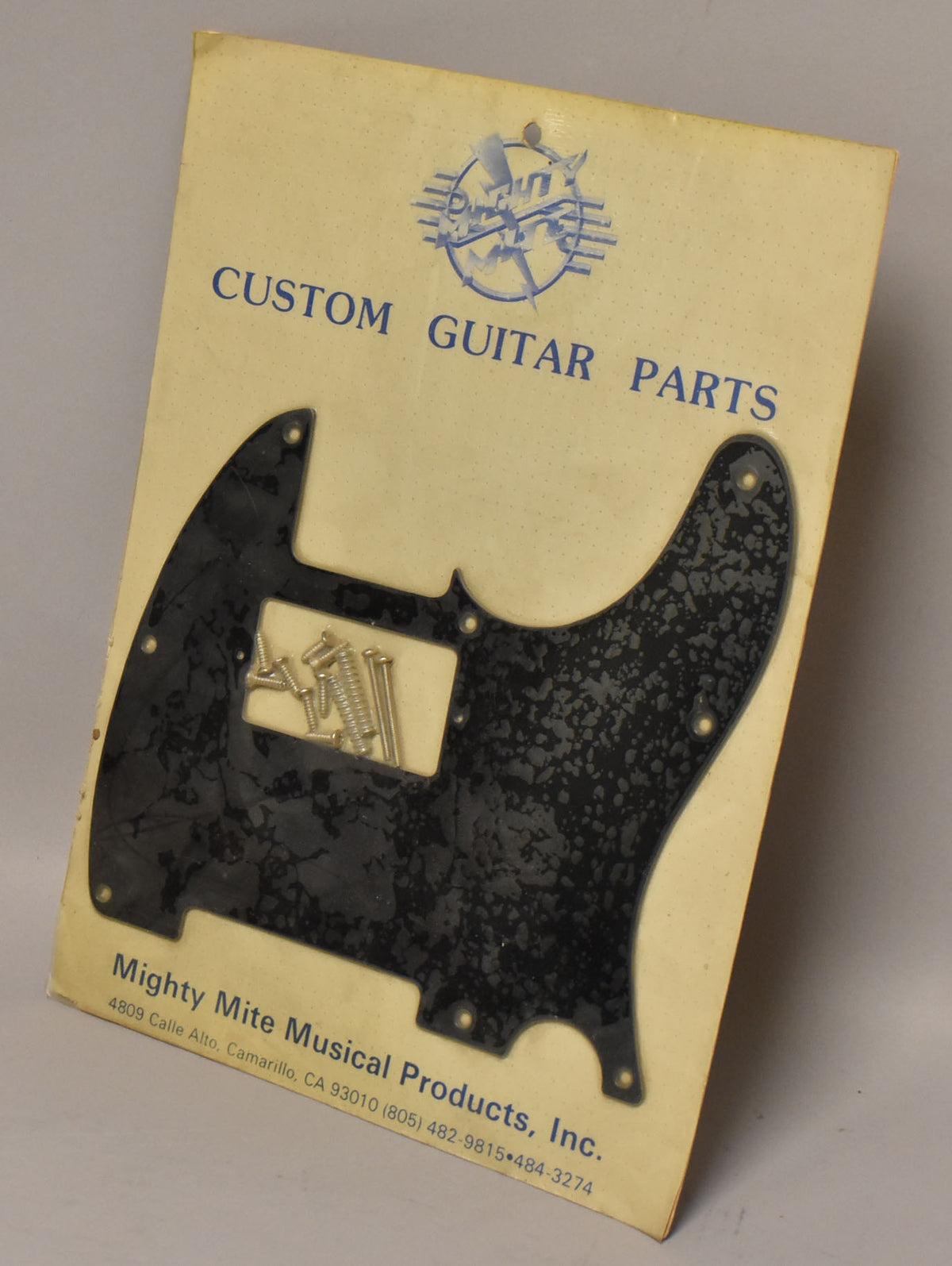 Black pickguard with a subtle mottled finish, sealed in original packaging with mounting screws, viewed from a slight angle.