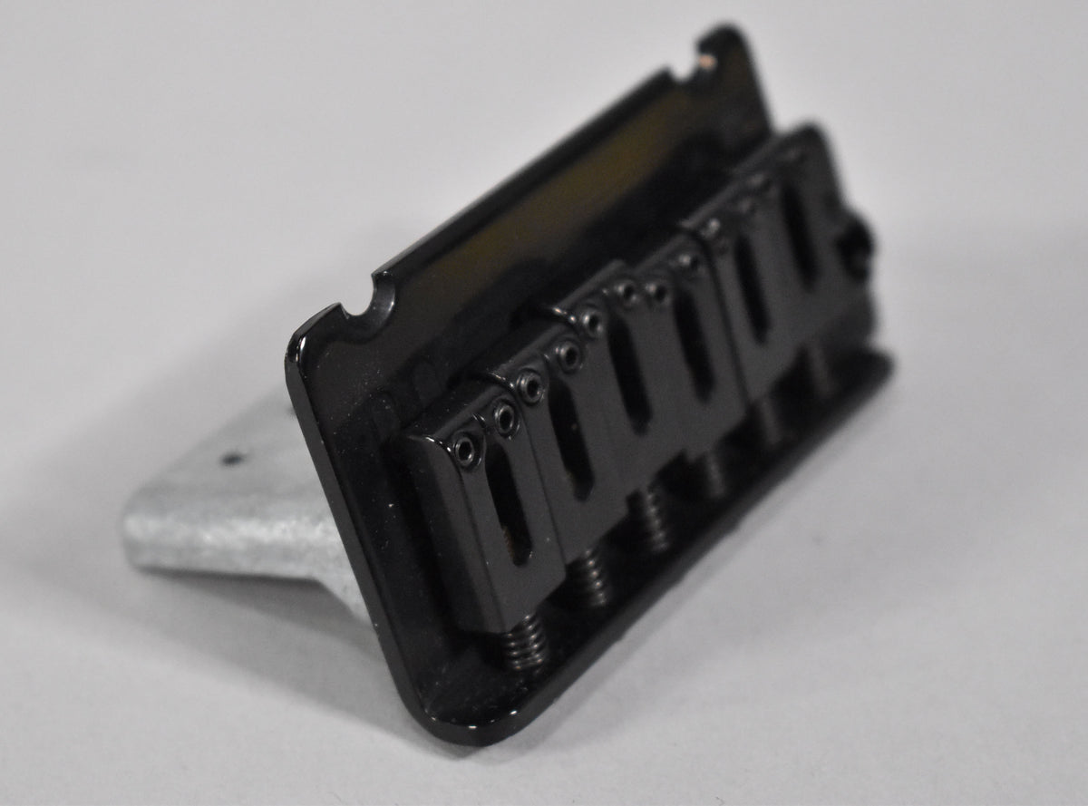 A black tremolo bridge, angled from the front right, showing six individual saddles with adjustment screws.