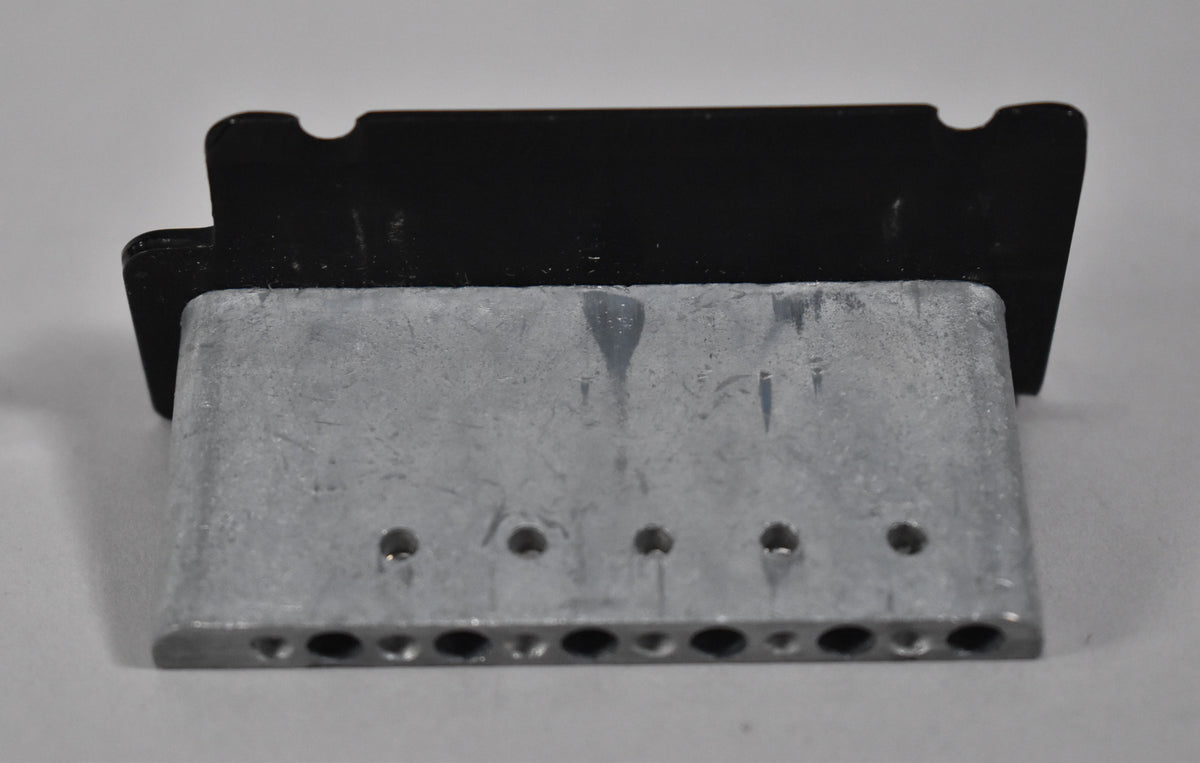 Rear view of the black tremolo block, showing six string holes and six smaller screw holes on the top surface.