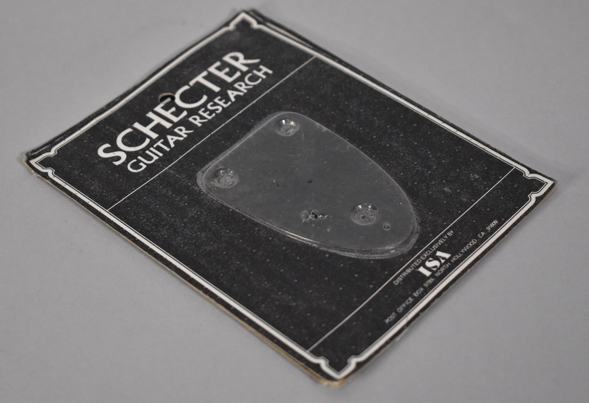 A clear, plastic guitar neck plate on a black Schecter Guitar Research card.