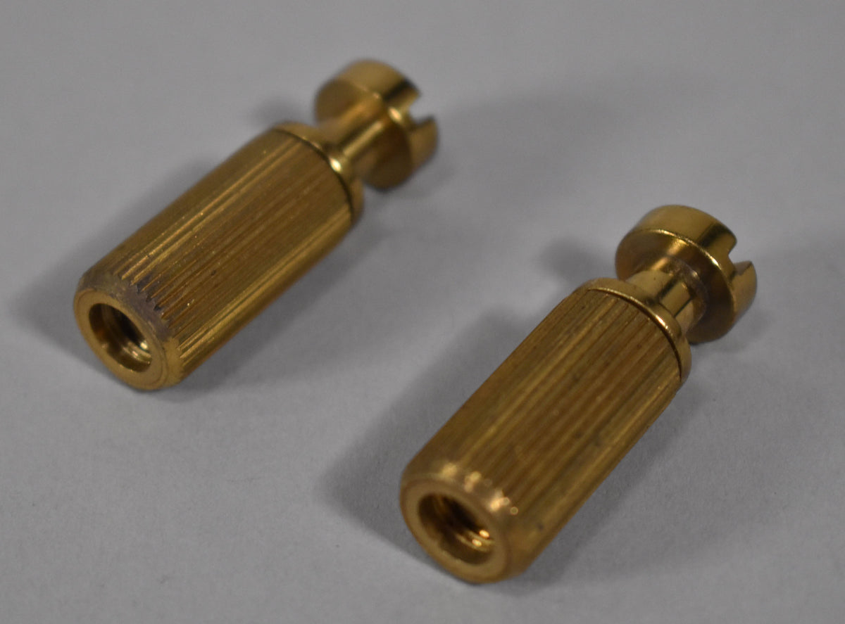 Two brass stoptail studs and bushings, with vertical knurling and slotted tops, angled on a light gray surface.