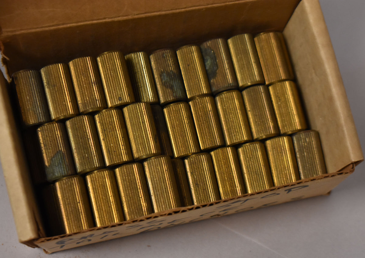 A top-down view of many brass bridge studs with vertical grooves, some showing dark green oxidation, in a cardboard box.