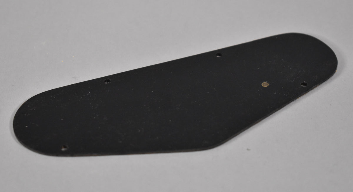Black plastic control cavity back plate, viewed from above, with four screw holes and a small brass-colored grommet.