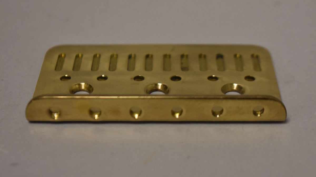 A gold hardtail bridge plate, viewed from the front, showing six string-through holes and six saddle mounting holes.