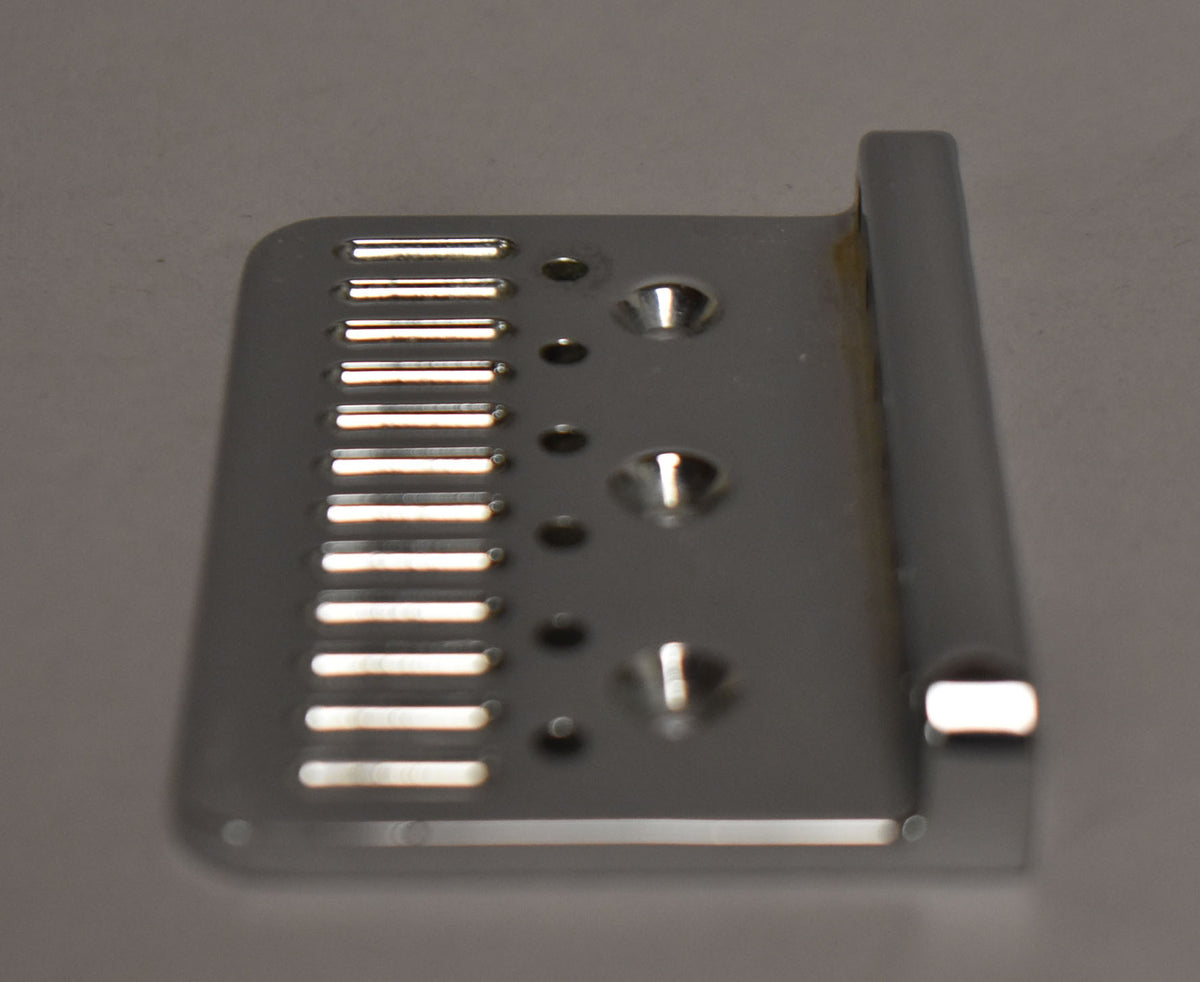 A chrome hardtail bridge plate, viewed from above, shows six string slots, three mounting holes, and some light tarnishing.