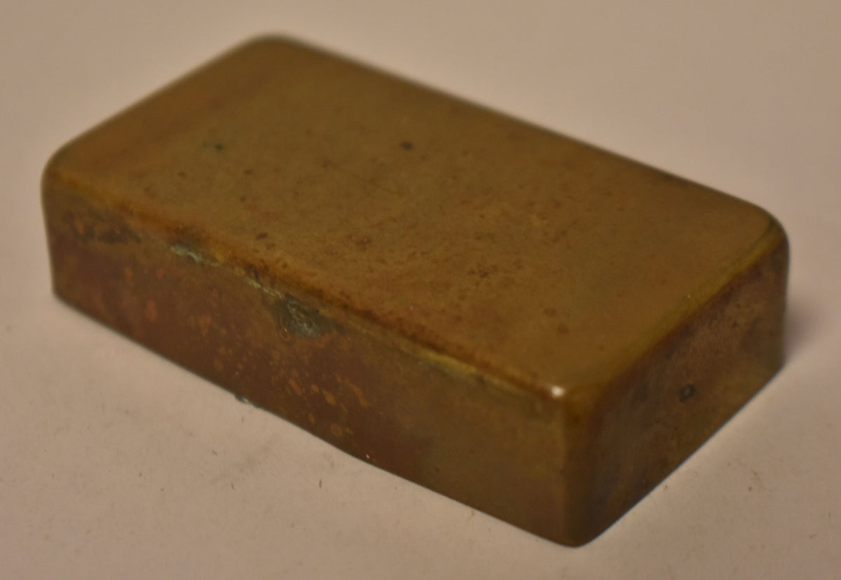 A single, rectangular gold brass humbucker cover is shown from a high angle, revealing a heavily tarnished and worn finish.