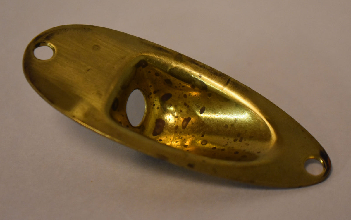 A gold brass football-shaped input jack cup, viewed from above, shows heavy tarnishing and two screw holes.
