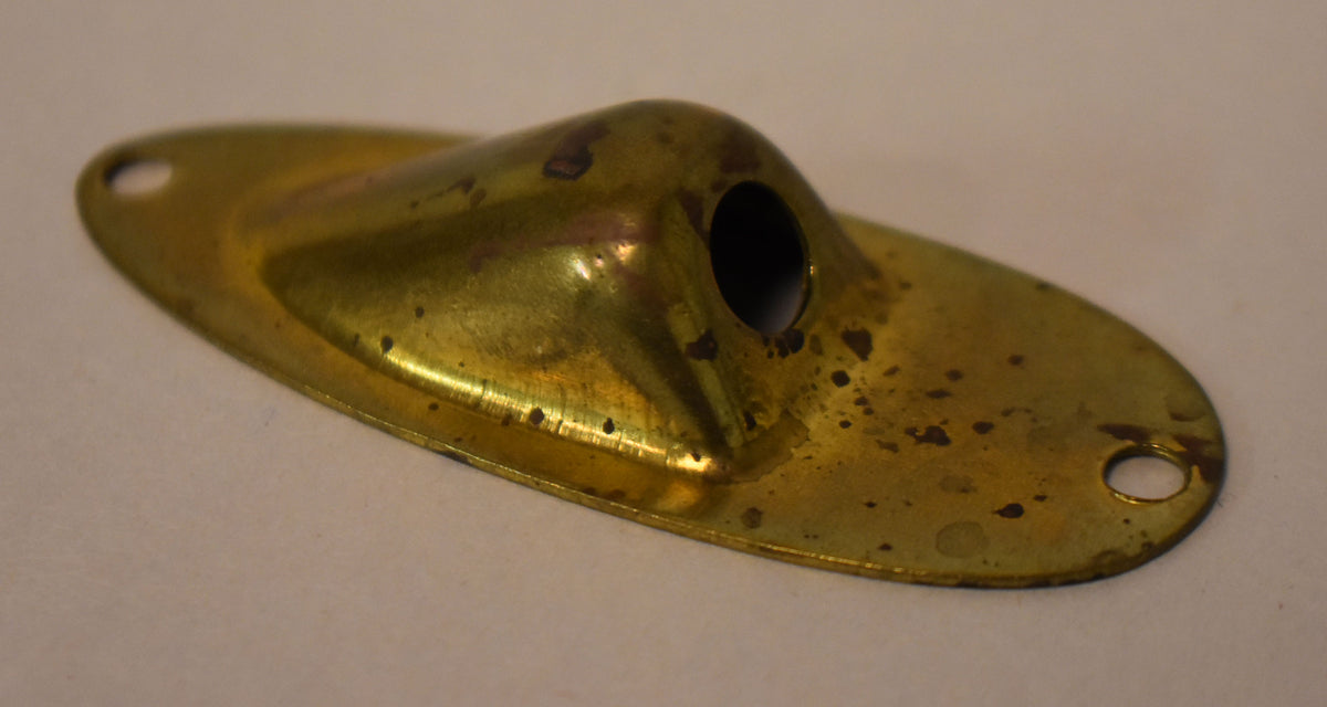 A tarnished gold brass input jack cup, viewed from above, shows dark spots and a worn finish, with two screw holes visible.