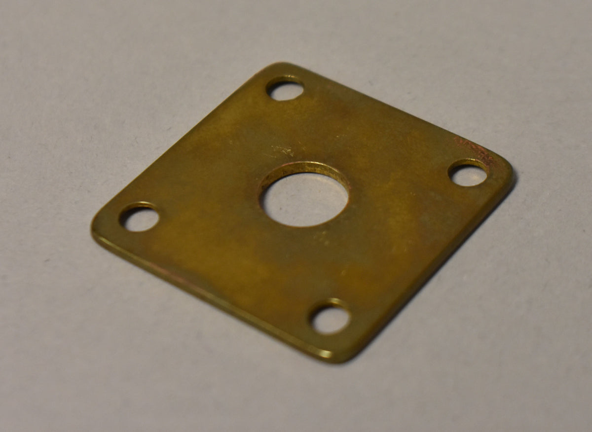 A square brass input jack plate with a central hole and four corner screw holes, showing some tarnishing.