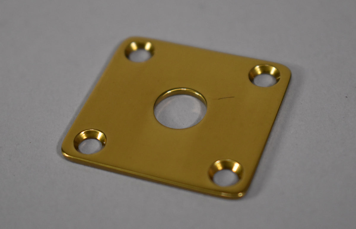Square, polished brass input jack plate with a central hole and four countersunk screw holes, viewed from a slight angle.