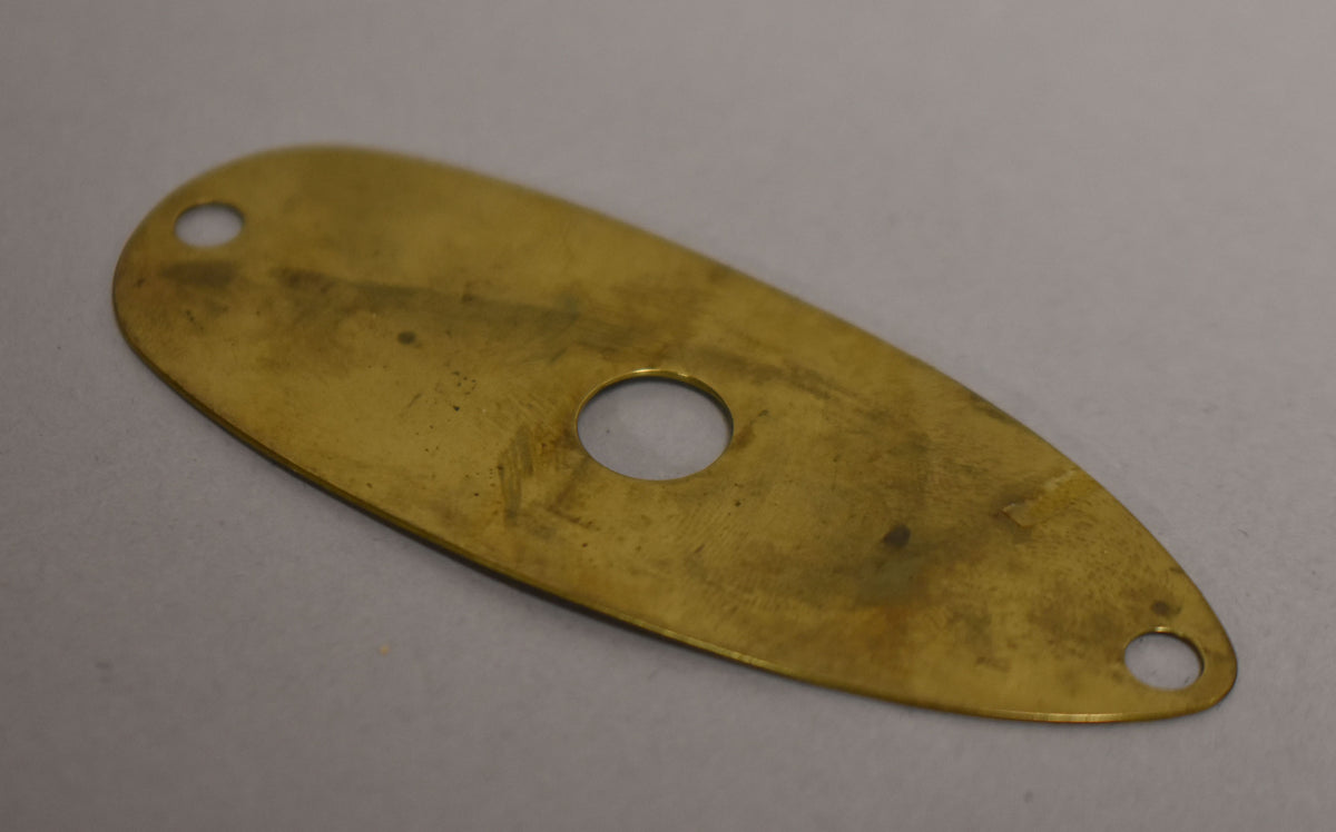 A brass input jack plate, viewed from above, with a central circular hole and two smaller screw holes at each end.
