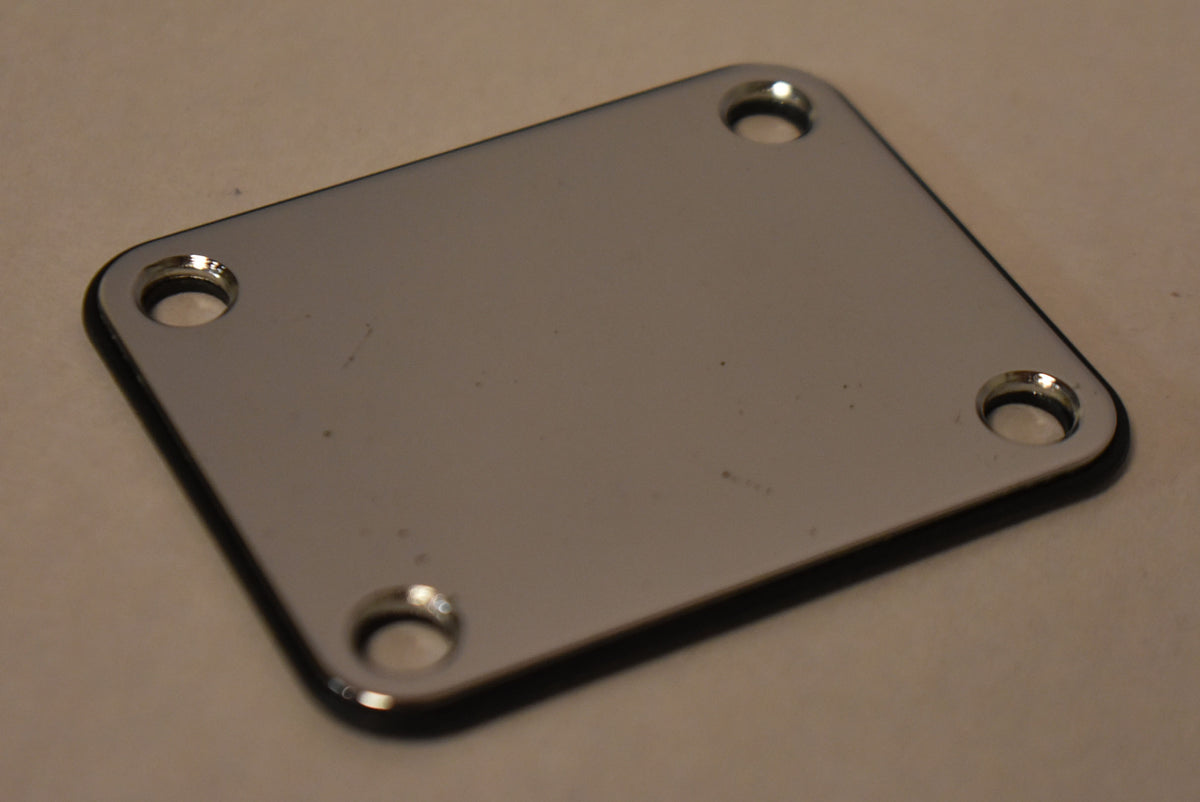 A rectangular chrome neck plate with four screw holes, viewed from above at an angle, showing the black gasket underneath.