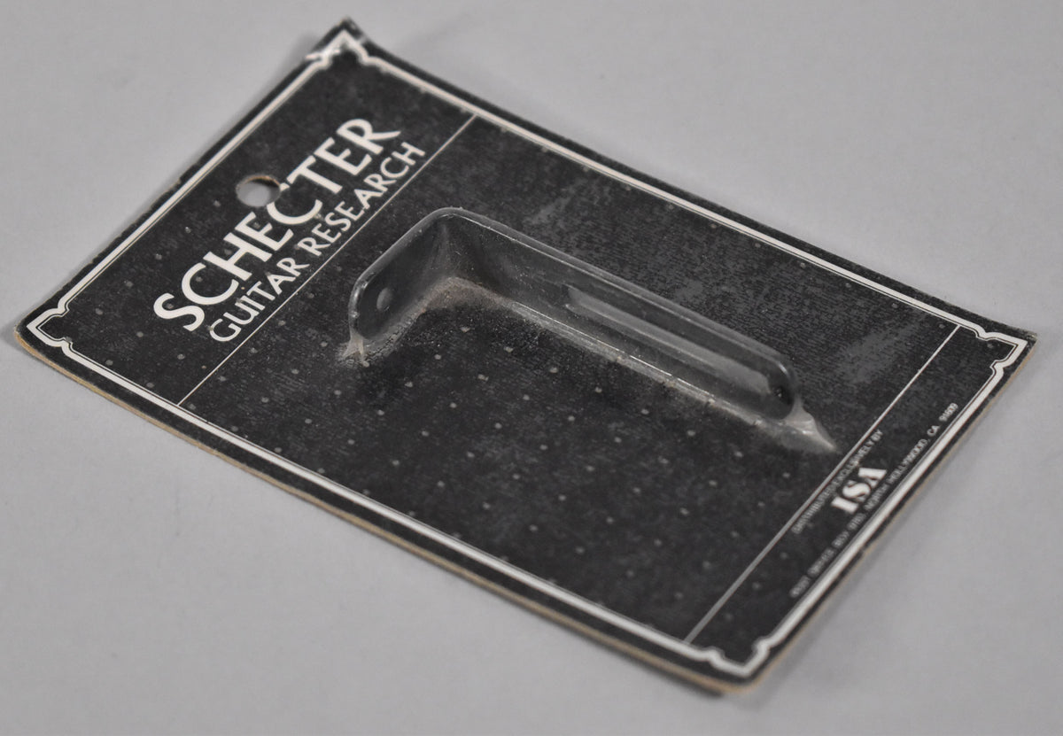 A black L-shaped pickguard bracket with a mounting hole, sealed in clear plastic on a black and white card.
