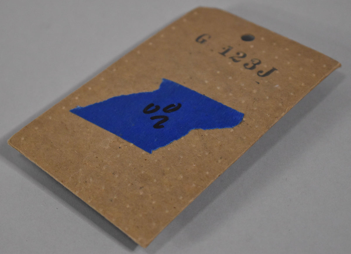 The black pickguard mounting bracket is sealed in its original brown paper packaging with a blue label and handwritten numbers.
