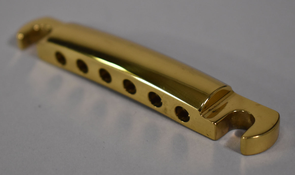 The polished gold brass tailpiece is angled, showing its six string-through holes and the curved hook on the right end.