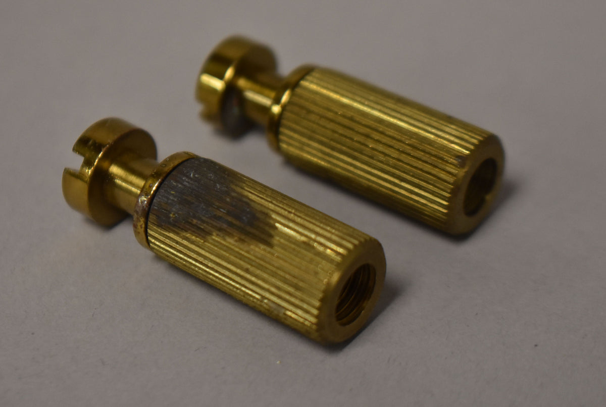 Two gold brass stop tailpiece studs and bushings, one with dark oxidation and a visible threaded interior.