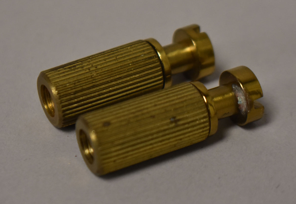 Two gold-colored brass stop tailpiece studs and bushings, with visible tarnishing and wear on the slotted heads.