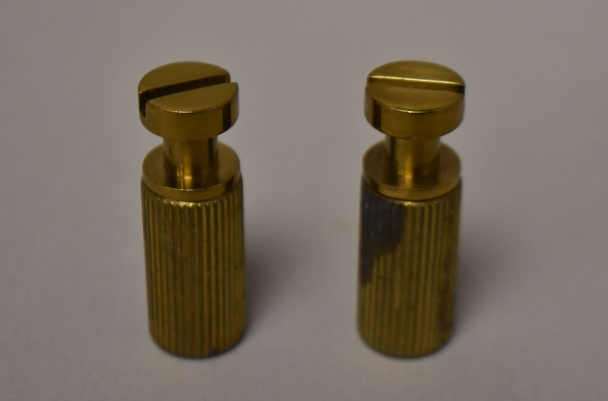 Two gold-colored brass studs with slotted tops and ribbed bushings, one showing dark discoloration on its side.