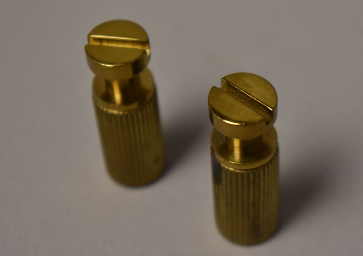 Two gold-plated brass stop tailpiece studs with slotted tops and ribbed sides, viewed from above at an angle.