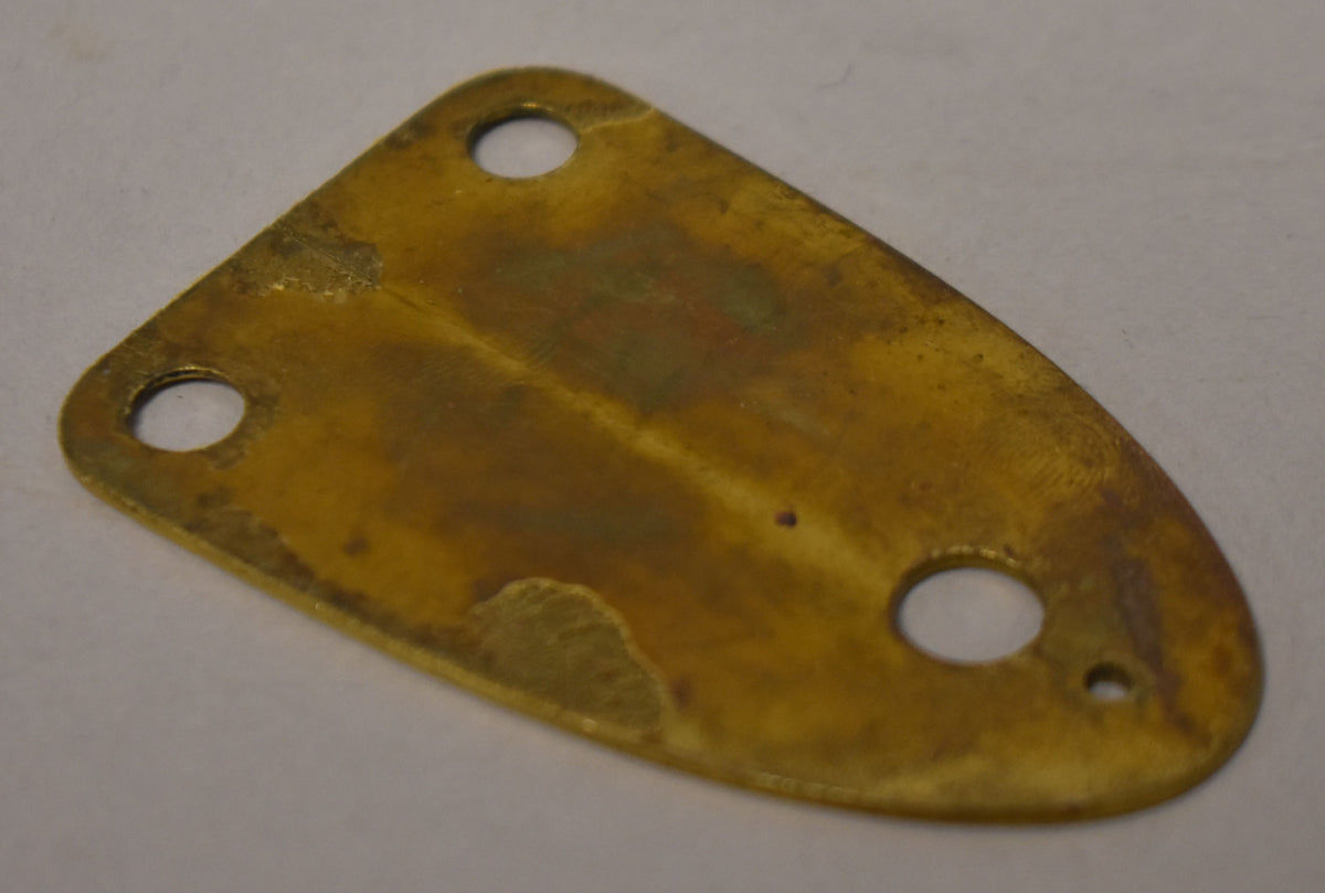 A brass 3-bolt neck plate, viewed from above, shows a dark patina with areas of green oxidation and a small, dark spot near the center.