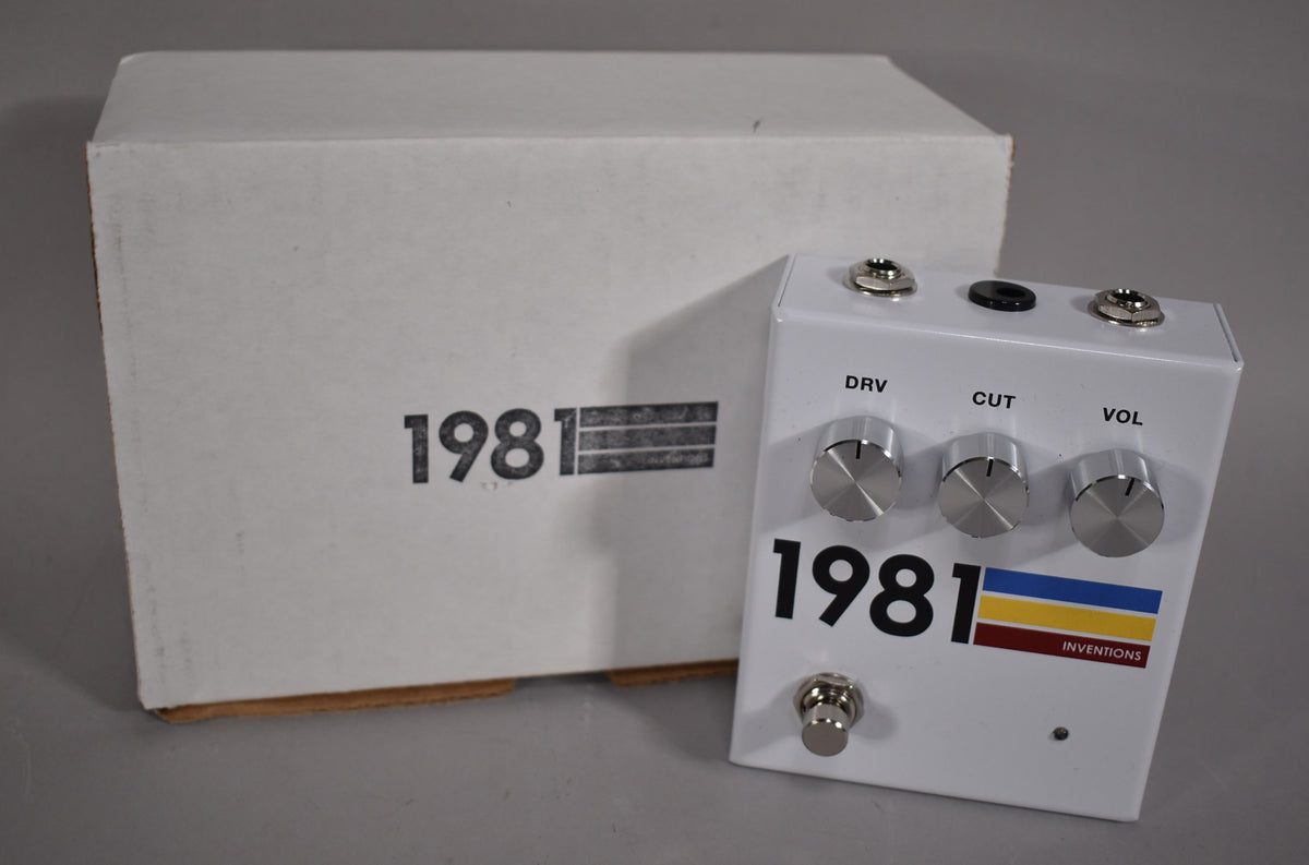 White pedal with three silver control knobs labeled DRV, CUT, and VOL, a footswitch, and three jacks on top, next to its white box.