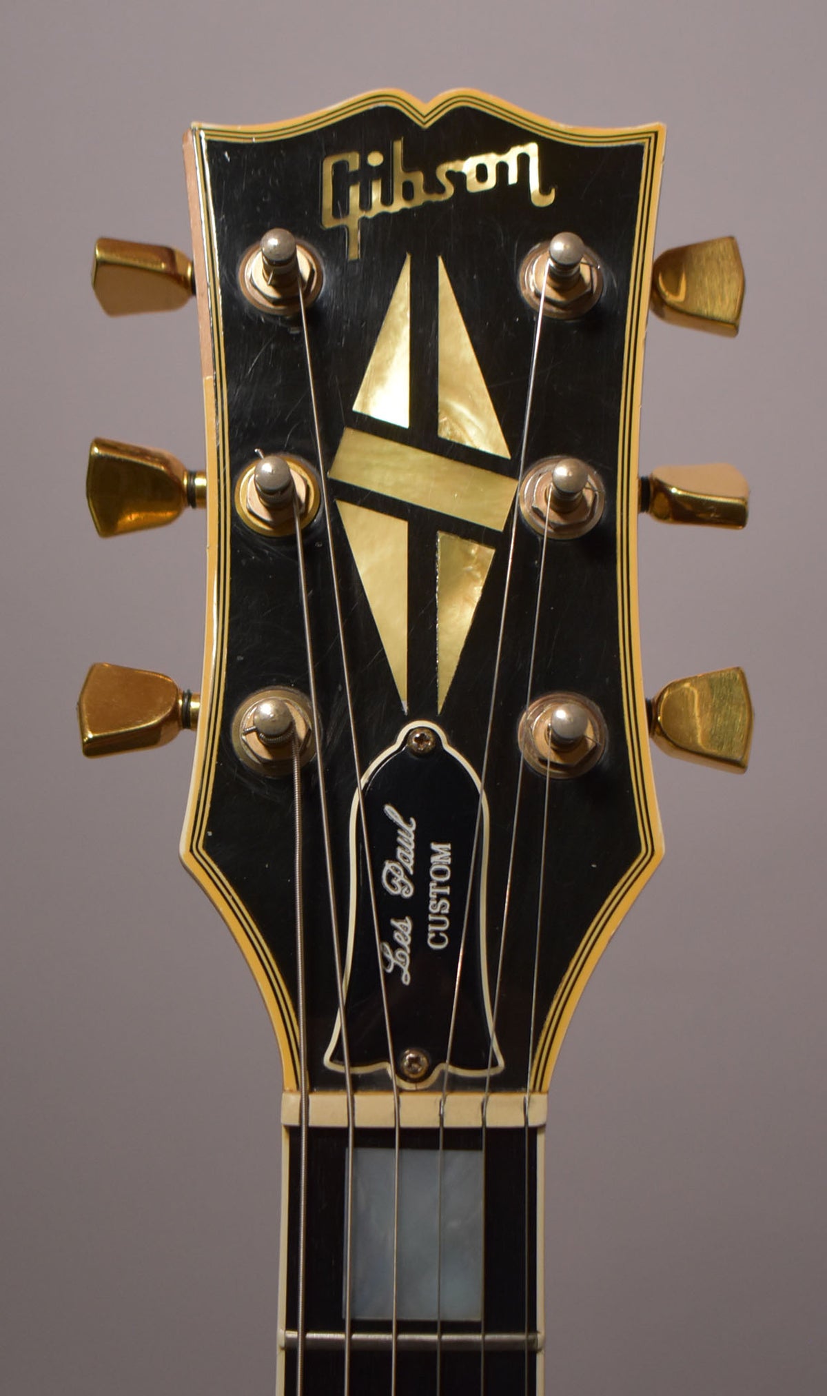 Close-up of the black headstock with gold tuners, mother-of-pearl inlay, and a white-bound neck with rectangular inlays.