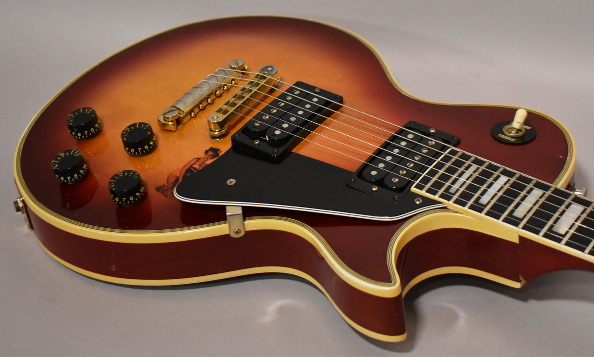 Close-up of the cherry sunburst body, showing gold hardware, black pickups, four black control knobs, and a pin-up girl decal.