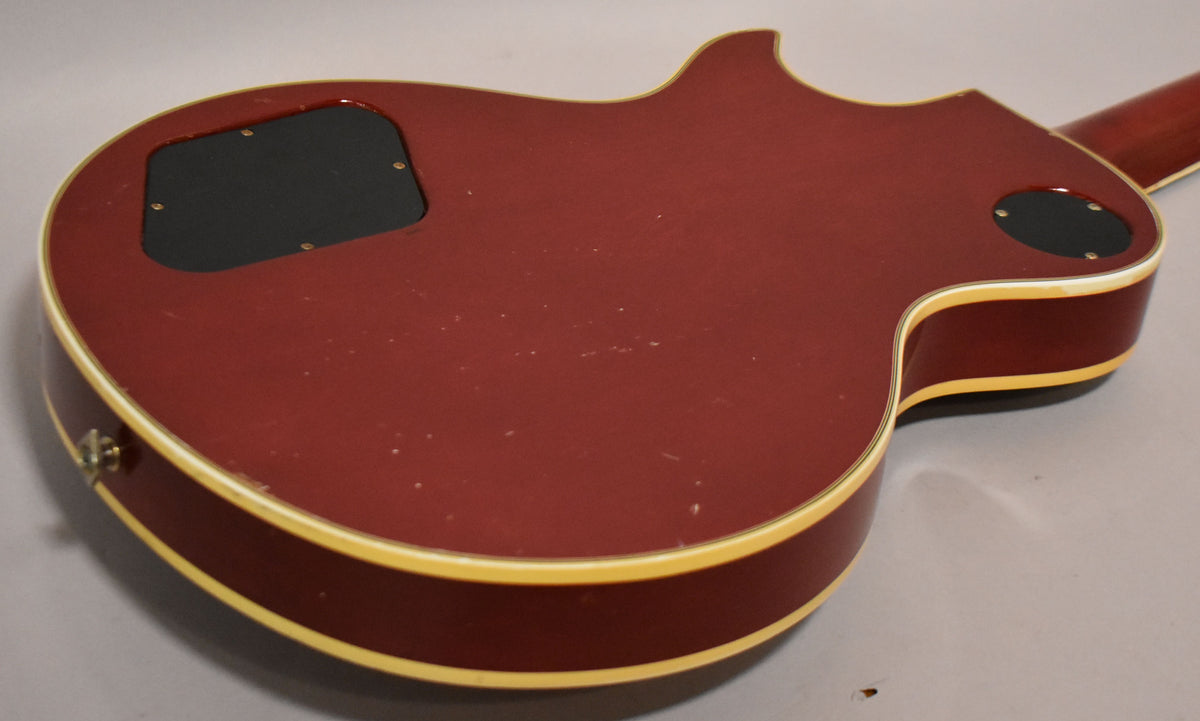 The back of the cherry sunburst guitar shows light scratches, a control cavity cover, and a jack plate, all framed by cream binding.