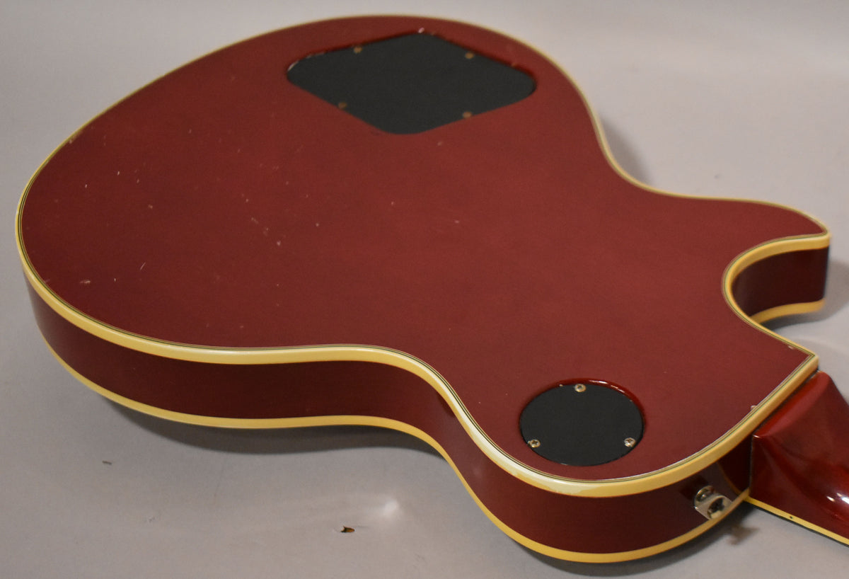 The back of a cherry sunburst electric guitar, showing two black control cavity covers and light surface wear.
