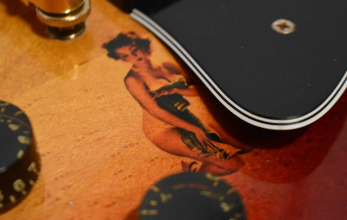 Close-up of the cherry sunburst body with a pin-up girl decal, two black speed knobs, and a multi-ply pickguard.