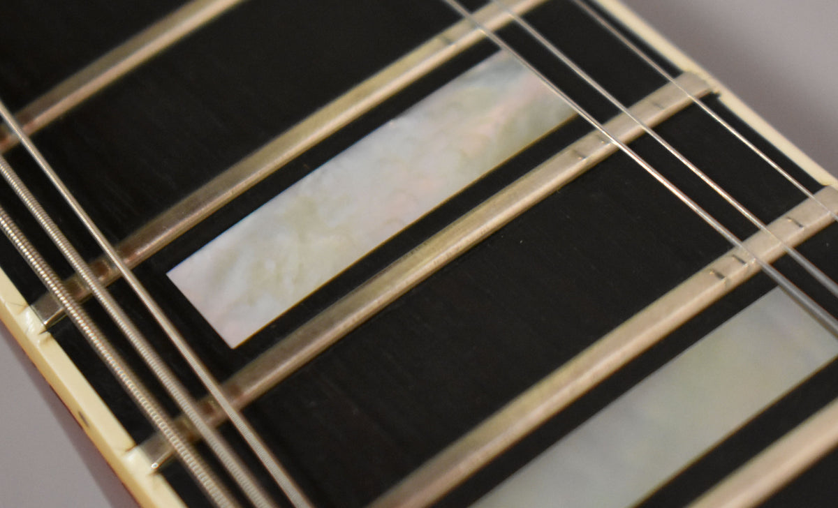 Close-up of the dark fretboard with rectangular mother-of-pearl inlays, showing light wear on the frets and strings.