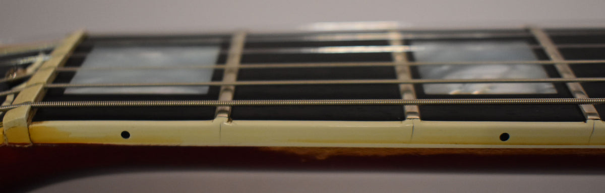 Close-up of the guitar's fretboard from the side, showing cream binding with dark side dots, trapezoid inlays, and light fret wear.