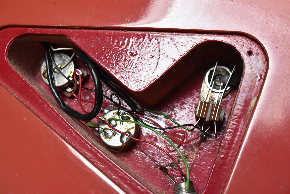 Close-up of the guitar's control cavity, revealing two potentiometers, a 3-way switch, and wiring against the faded pink finish.
