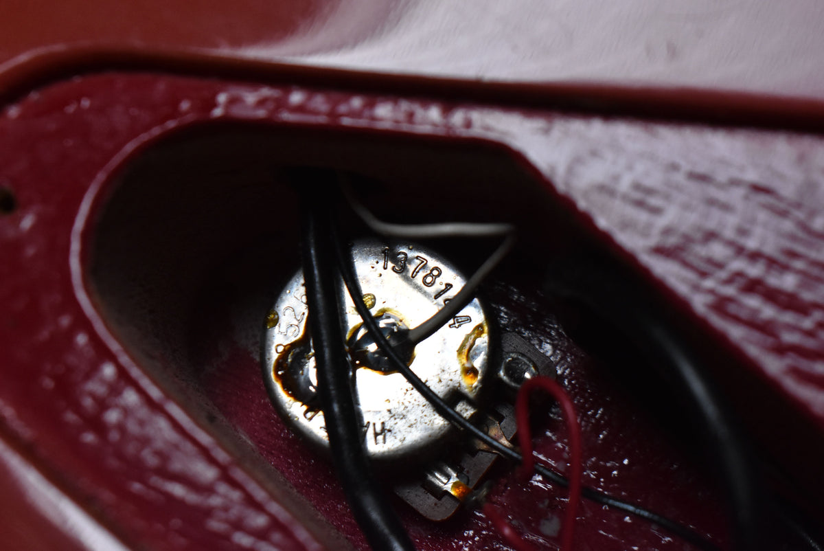 Close-up of the guitar's control cavity, revealing a potentiometer with visible wiring and solder joints, surrounded by the faded pink finish.