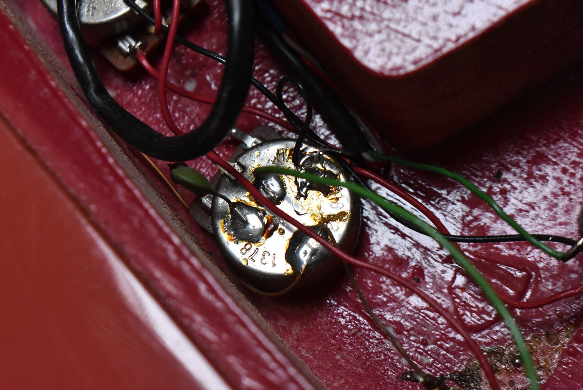 Close-up of the guitar's wiring cavity, showing a potentiometer with visible solder joints and various colored wires against the faded pink finish.