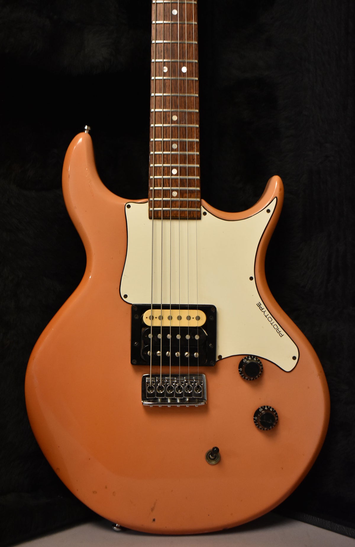 The faded pink electric guitar's body and lower neck are visible, showing a single humbucker, two knobs, and a white pickguard.