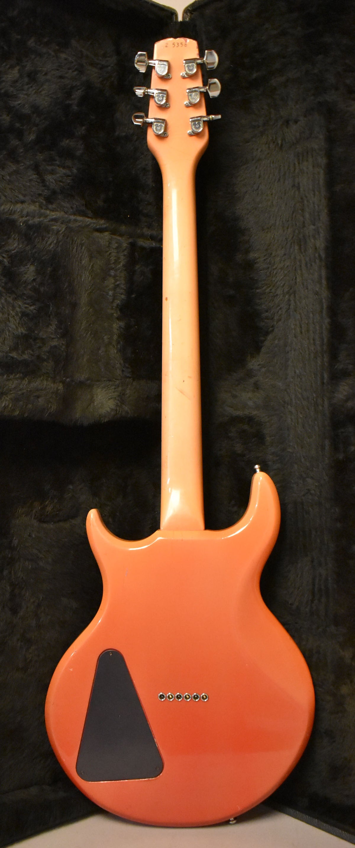 The back of a faded pink electric guitar, showing the headstock with six tuners, neck, and body with a black triangular plate.