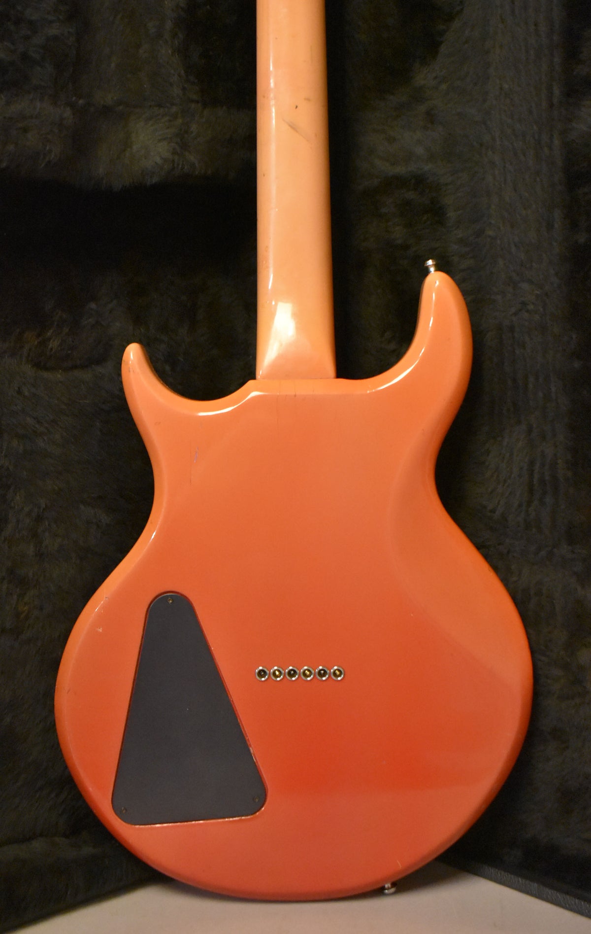 The guitar's faded pink back, with a black triangular control cavity cover and six string-through ferrules, shows light wear.
