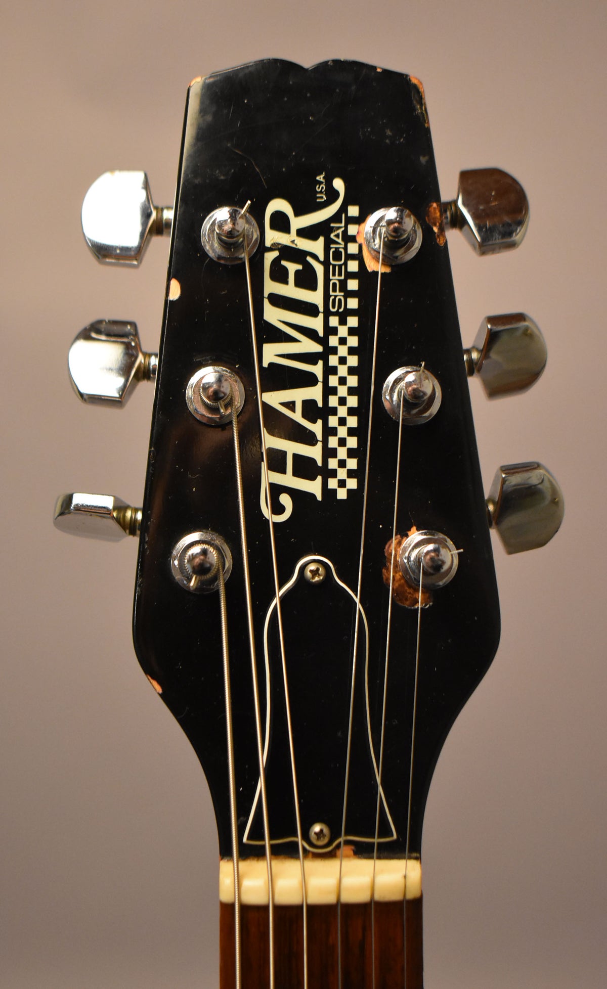 Close-up of the black headstock with six chrome tuners, showing finish wear and chips around the edges and tuners.