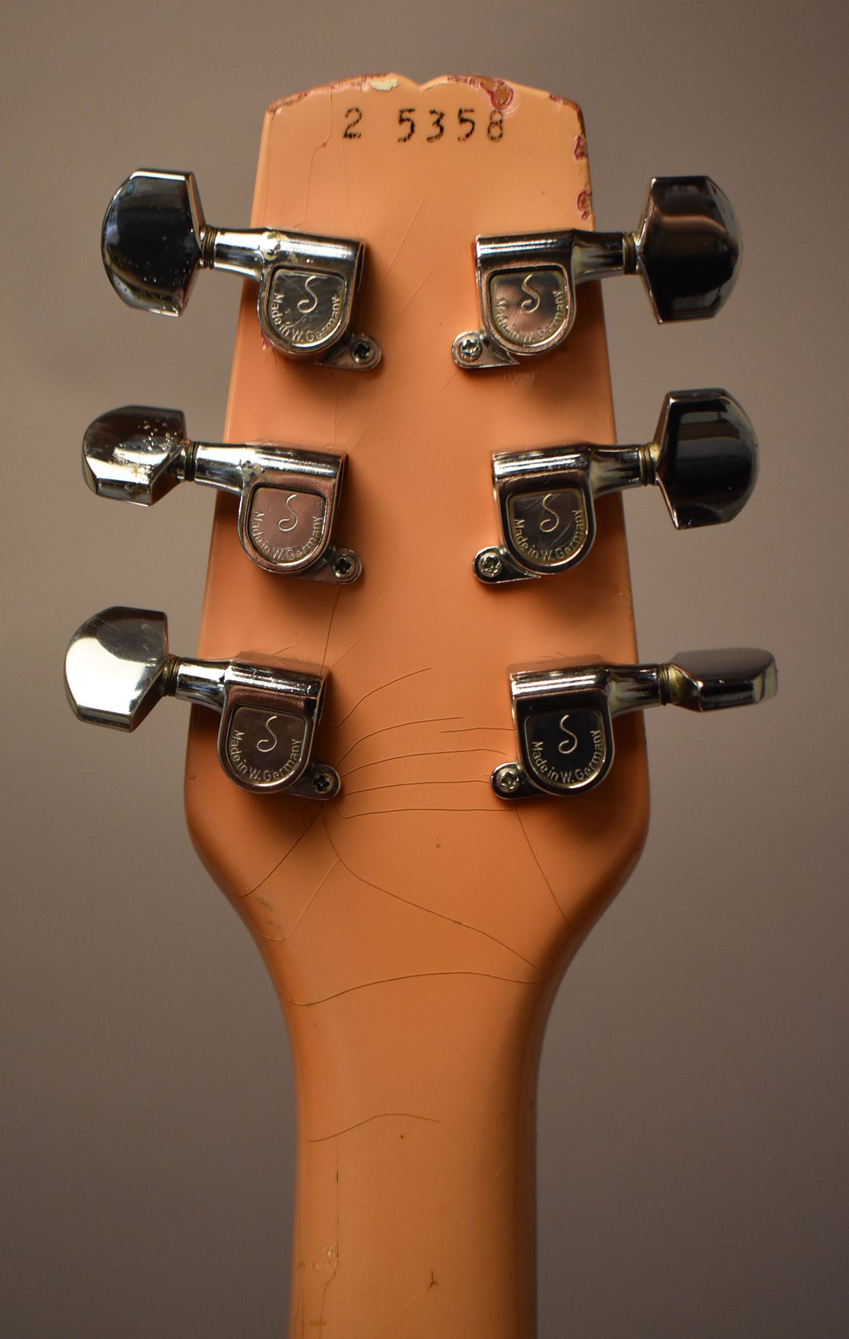 The back of a faded pink headstock with six chrome tuners, showing extensive finish checking and wear around the edges.