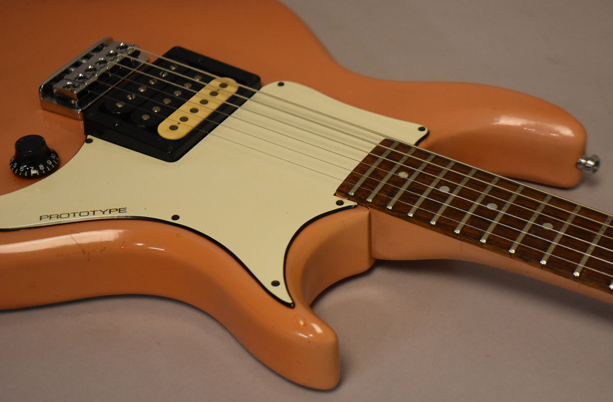 Close-up of a faded pink electric guitar body with a white pickguard, black humbucker, cream single-coil, and a volume knob.
