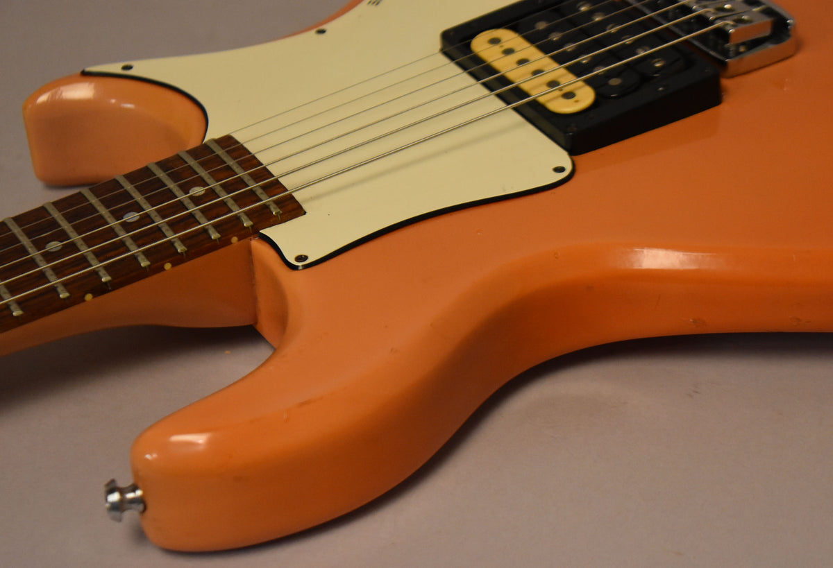 Close-up of the faded pink guitar body and neck joint, showing a cream pickguard, a single humbucker, and finish wear.