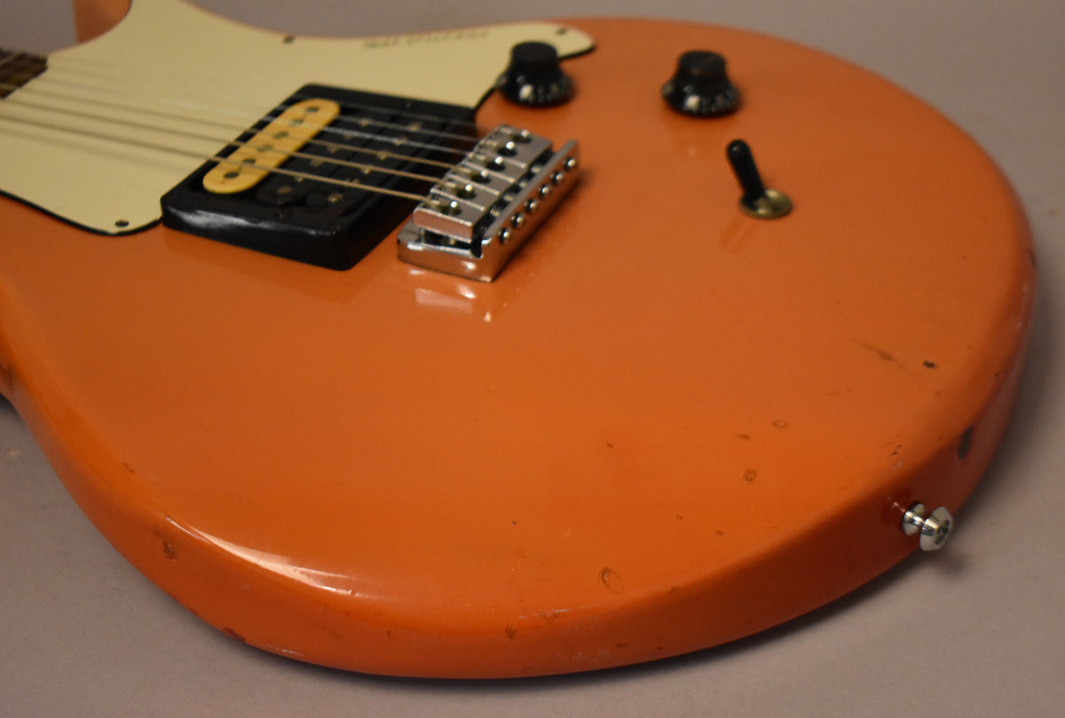 Close-up of the faded pink guitar body, showing a single humbucker, tune-o-matic bridge, two black knobs, and a toggle switch.