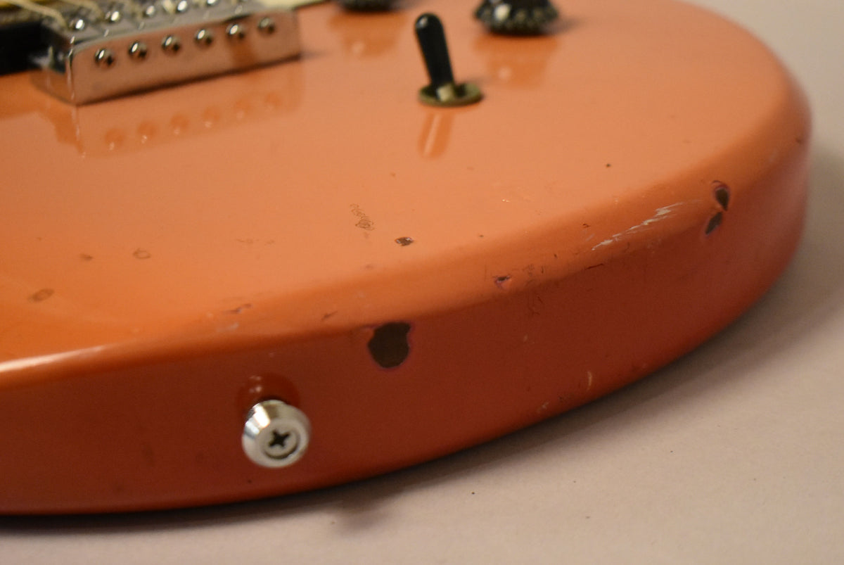 Close-up of the guitar's faded pink body, showing a chrome strap button, a black switch, and several chips and scratches.
