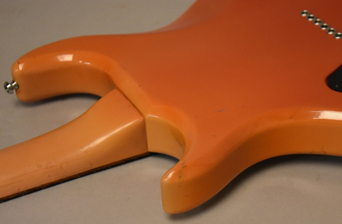 The guitar's faded pink body and neck joint show visible wear, nicks, and finish checking, with a strap button on the lower horn.