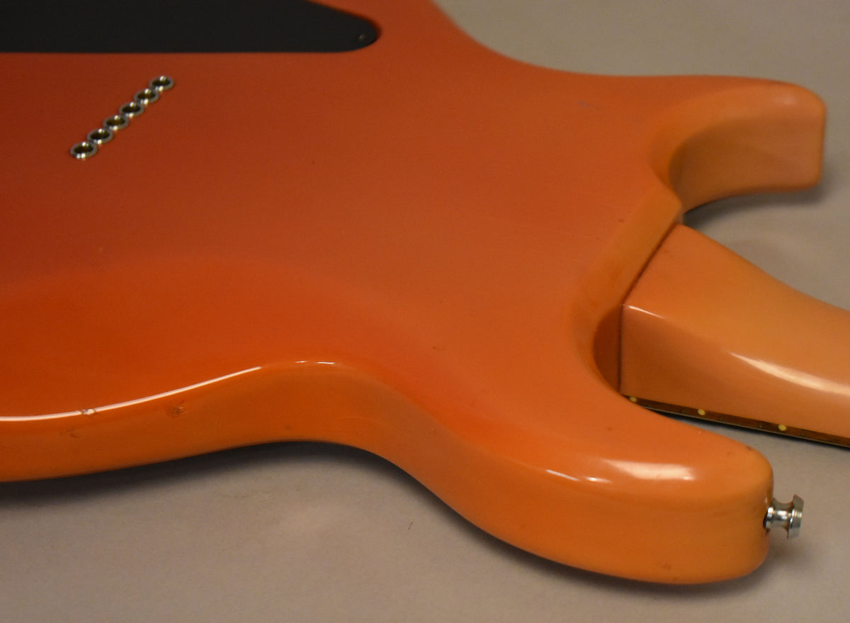 The faded pink guitar body, viewed from the back, shows a six-saddle string-through-body bridge and a few small dings.