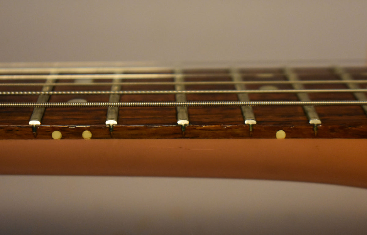 Close-up of the dark rosewood fretboard and frets, showing side dots and some wear on the fretboard edges.